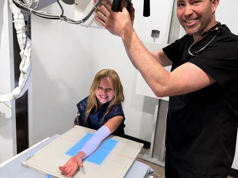 Dr. McRae positioning the digital X-ray tube over a young patient’s forearm in the on-site imaging room